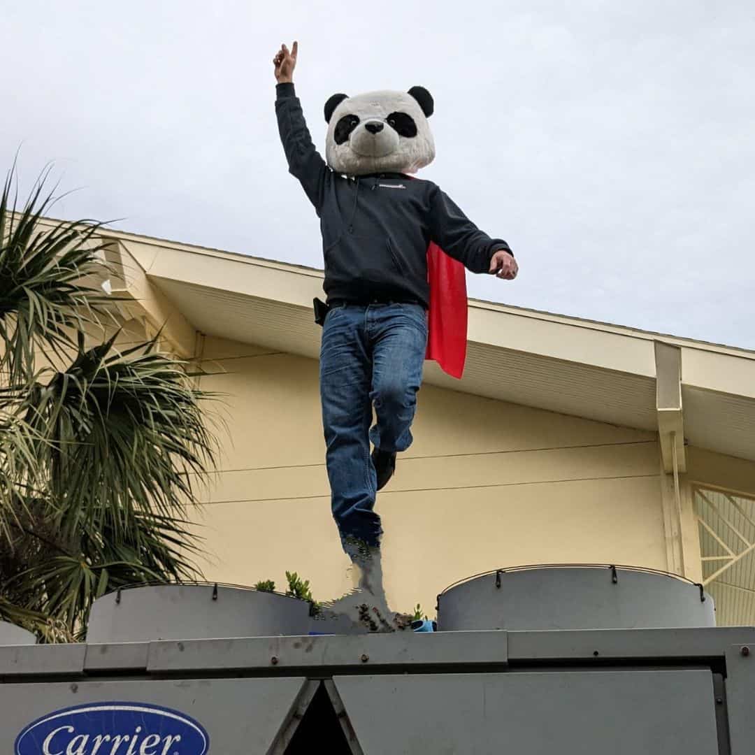 AC Panda mascot standing on an Air Conditioner Unit triumphantly